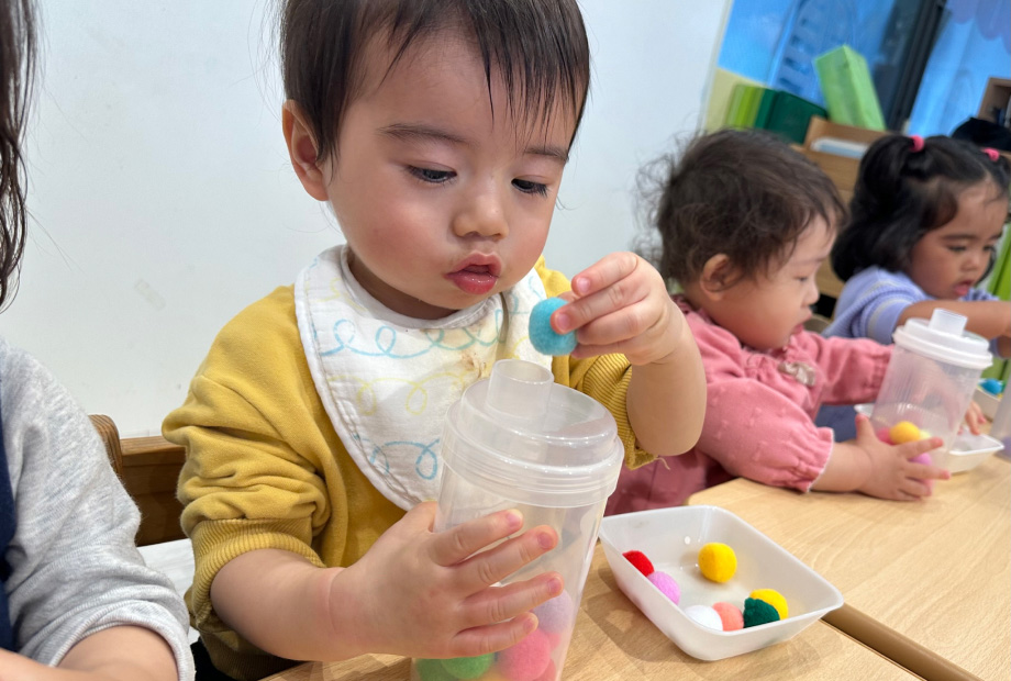小さな穴にポンポンを入れる指先を使う遊びに真剣に取り組む子どもの写真