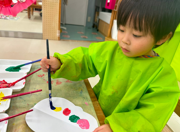 たくさんの色の絵の具を使用して、絵を描く子どもの写真