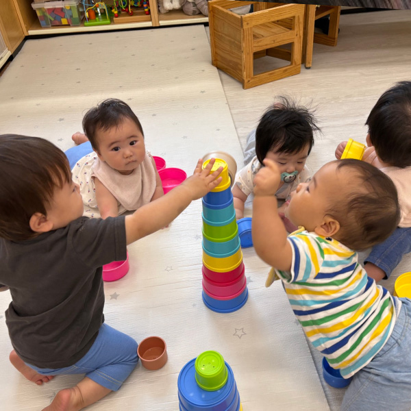 みんなで一つのおもちゃを囲んで遊ぶ0歳児の写真